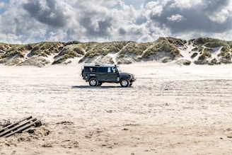A rugged Jeep Wrangler parked on a sandy beach with waves crashing in the background.