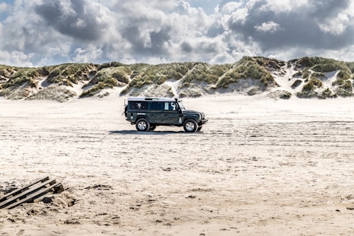 A rugged Jeep Wrangler parked on a sandy beach with waves crashing in the background.