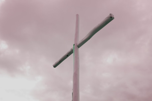 A rustic wooden cross standing tall against a cloudy sky.