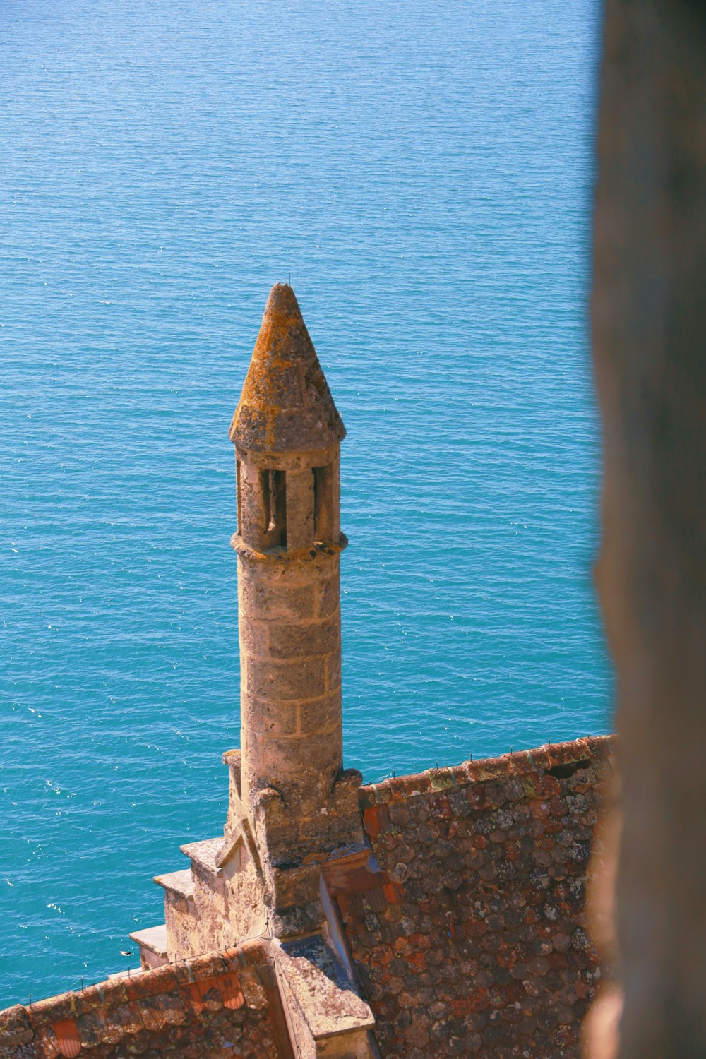 uma torre com um relógio no topo de um edifício ao lado de um corpo de água