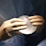 A pair of hands wearing surgical gloves holds a translucent, round, gel-like object, likely a medical implant. The background features a fabric that resembles surgical scrubs.