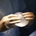 A pair of hands wearing surgical gloves holds a translucent, round, gel-like object, likely a medical implant. The background features a fabric that resembles surgical scrubs.