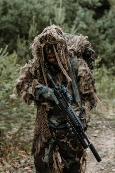 A rugged hunter in forest green gear carefully tracking through dense woodland at dawn.