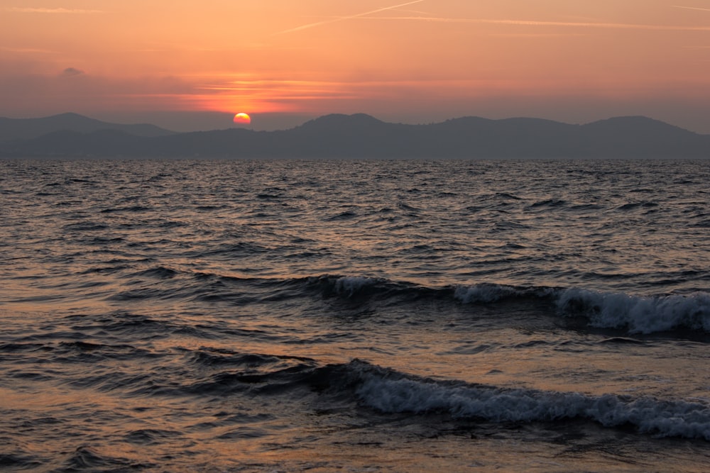 the sun is setting over the ocean with mountains in the distance