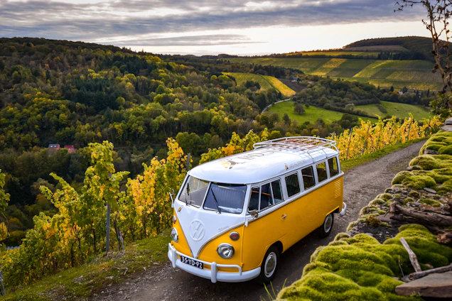 A charming vintage van parked on a sunlit Tuscan country road with rolling hills and vineyards in the background.
