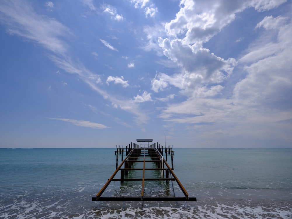 a long pier extending into the ocean under a cloudy blue sky