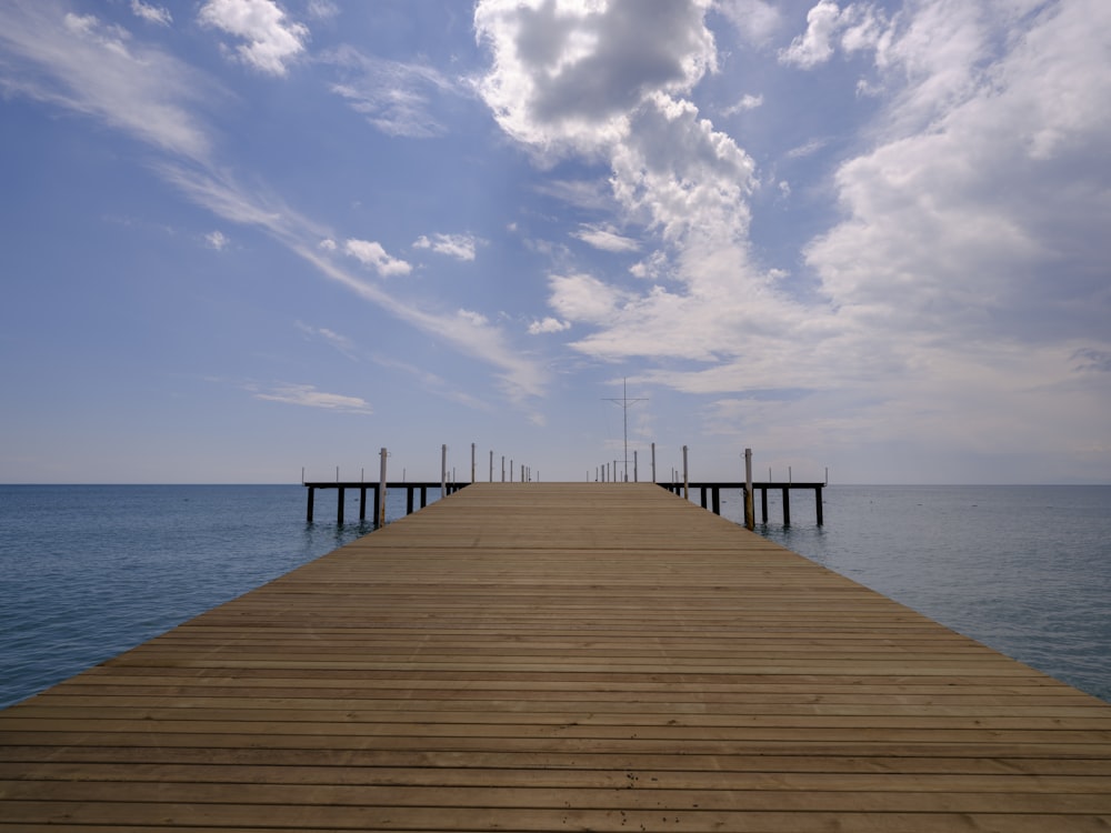 a wooden dock extending into the ocean under a cloudy blue sky