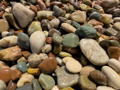 A collection of smooth, polished stones in various shapes and sizes, with a glossy finish. The stones feature a variety of colors, including hues of brown, green, white, and gray, creating a diverse and natural mosaic.