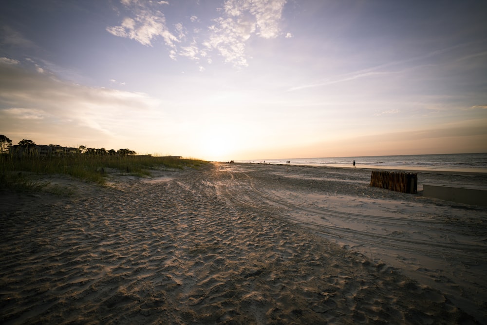 the sun is setting on the beach with the ocean in the background