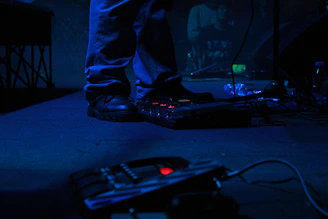 A musician testing a stomp box pedal on stage with colorful lighting.