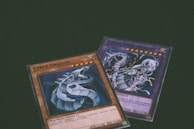Two trading cards from a collectible card game are displayed with a dragon theme. One card features the title 'Cyber Dragon', presenting an image of a metallic dragon with blue and silver hues. The second card, partially visible, also depicts a dragon with dynamic artwork involving purple and blue lightning effects.