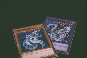 Two trading cards from a collectible card game are displayed with a dragon theme. One card features the title 'Cyber Dragon', presenting an image of a metallic dragon with blue and silver hues. The second card, partially visible, also depicts a dragon with dynamic artwork involving purple and blue lightning effects.