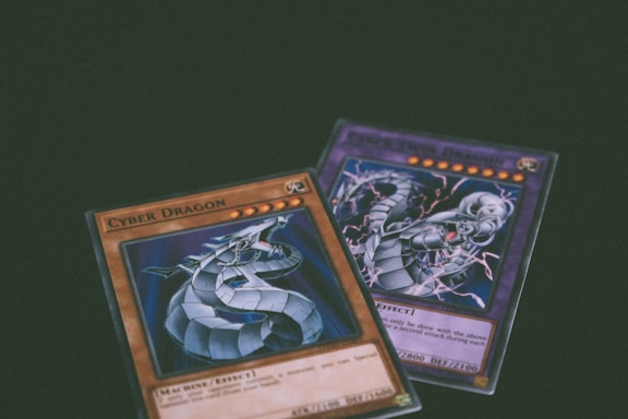 Two trading cards from a collectible card game are displayed with a dragon theme. One card features the title 'Cyber Dragon', presenting an image of a metallic dragon with blue and silver hues. The second card, partially visible, also depicts a dragon with dynamic artwork involving purple and blue lightning effects.