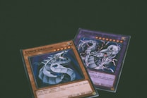Two trading cards from a collectible card game are displayed with a dragon theme. One card features the title 'Cyber Dragon', presenting an image of a metallic dragon with blue and silver hues. The second card, partially visible, also depicts a dragon with dynamic artwork involving purple and blue lightning effects.
