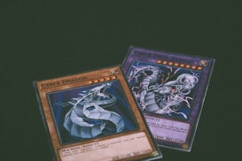 Two trading cards from a collectible card game are displayed with a dragon theme. One card features the title 'Cyber Dragon', presenting an image of a metallic dragon with blue and silver hues. The second card, partially visible, also depicts a dragon with dynamic artwork involving purple and blue lightning effects.
