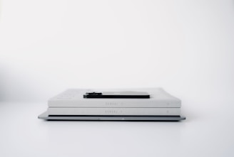 A minimalist scene featuring two identical light gray books stacked horizontally on a flat surface with a smartphone placed on top of them. The background is a clean white, enhancing the simplicity of the arrangement.