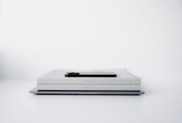 A minimalist scene featuring two identical light gray books stacked horizontally on a flat surface with a smartphone placed on top of them. The background is a clean white, enhancing the simplicity of the arrangement.