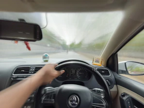 Driver's perspective showing hands on the wheel with a blurred urban background