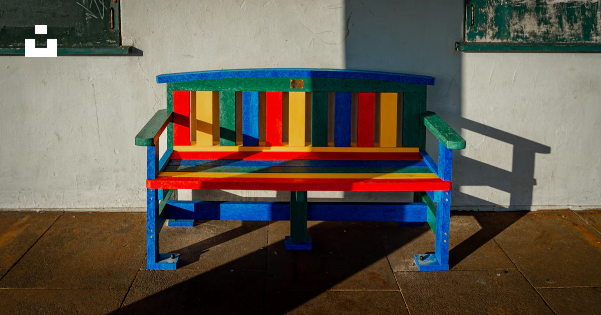 A brightly colored bench sitting in front of a building photo – Free ...