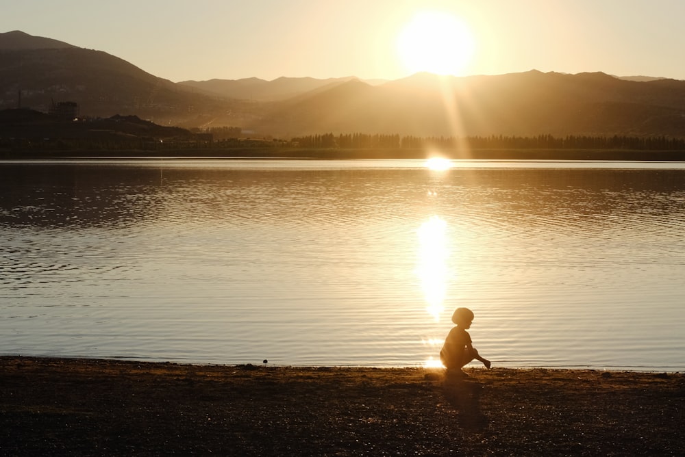 a person sitting on the shore of a lake at sunset