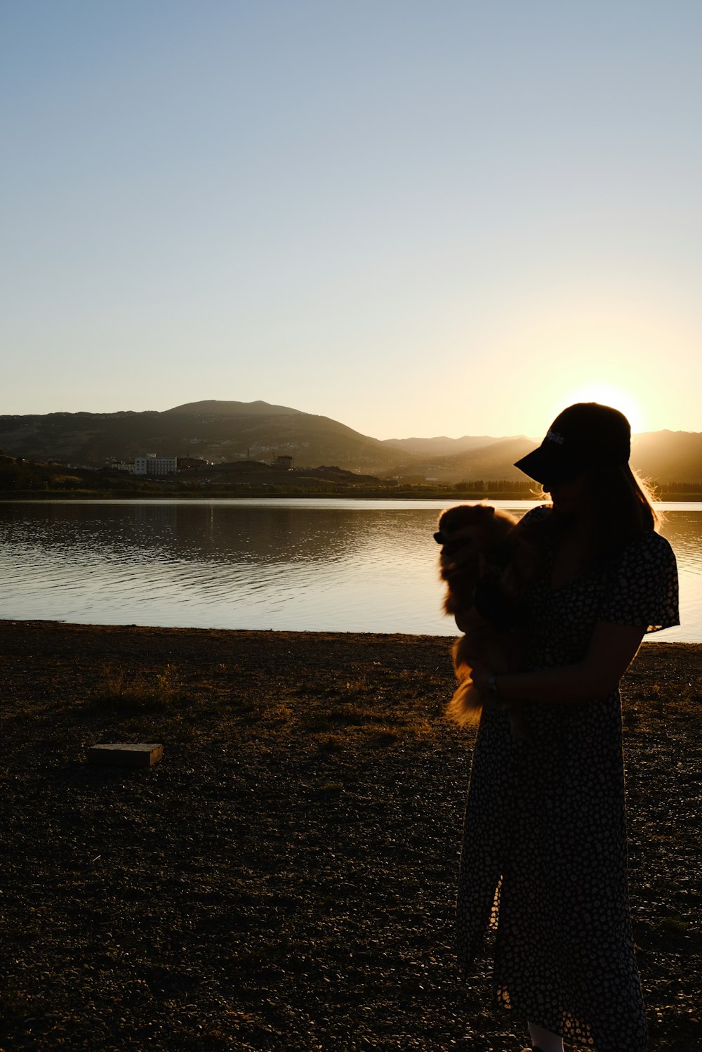 a woman holding a dog in front of a lake