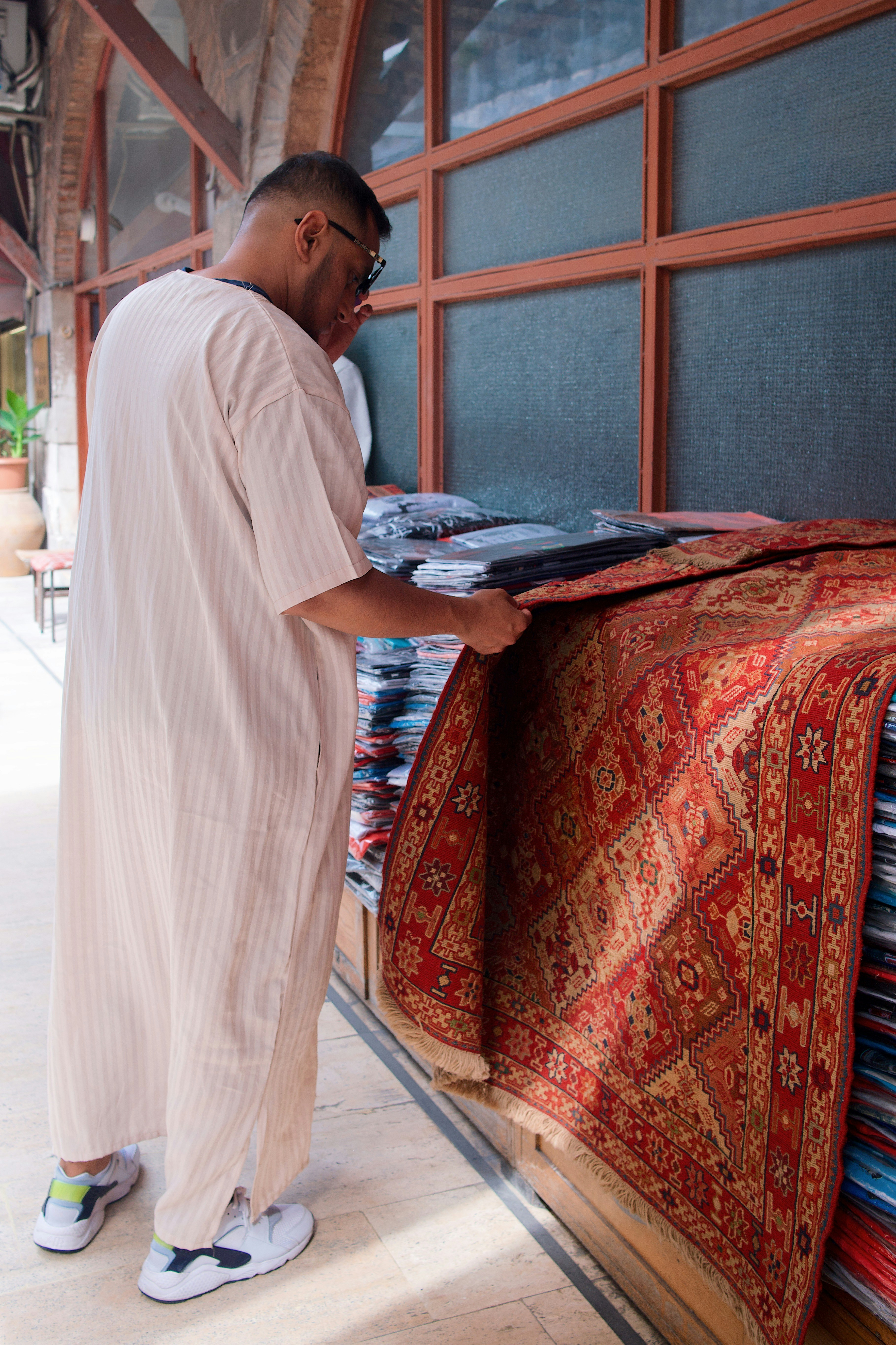 a man standing next to a pile of rugs