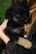 A small black and tan puppy is being held gently in a person's arms. The puppy looks calm and secure, nestled against the person's chest, with its head resting comfortably. The person's arm is wrapped around the puppy, providing a sense of protection. The background is softly blurred, focusing the attention on the tender interaction between the person and the puppy.