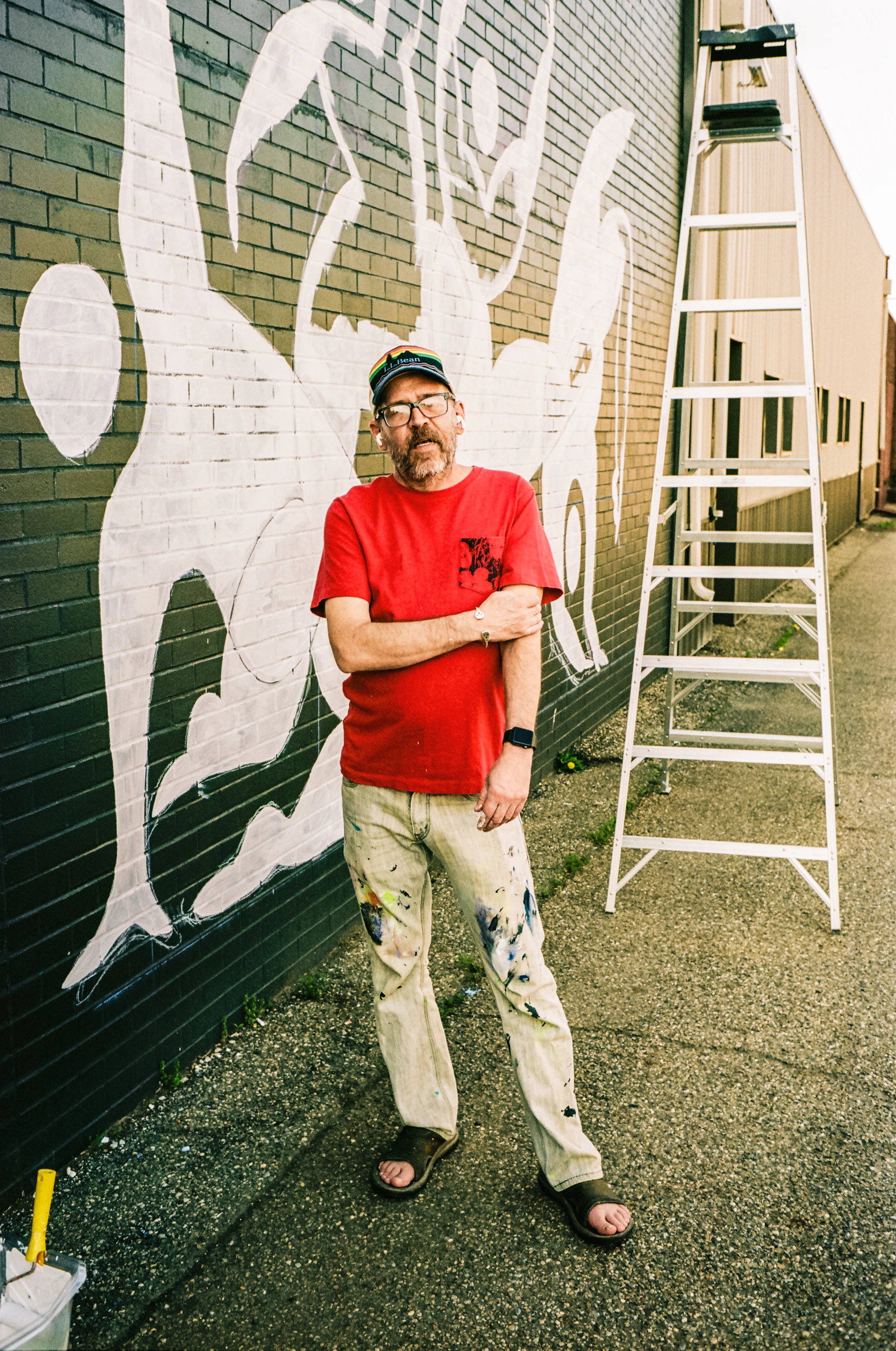A candid portrait of a local artist painting a mural on a brick wall, surrounded by tools and splashes of bright paint.