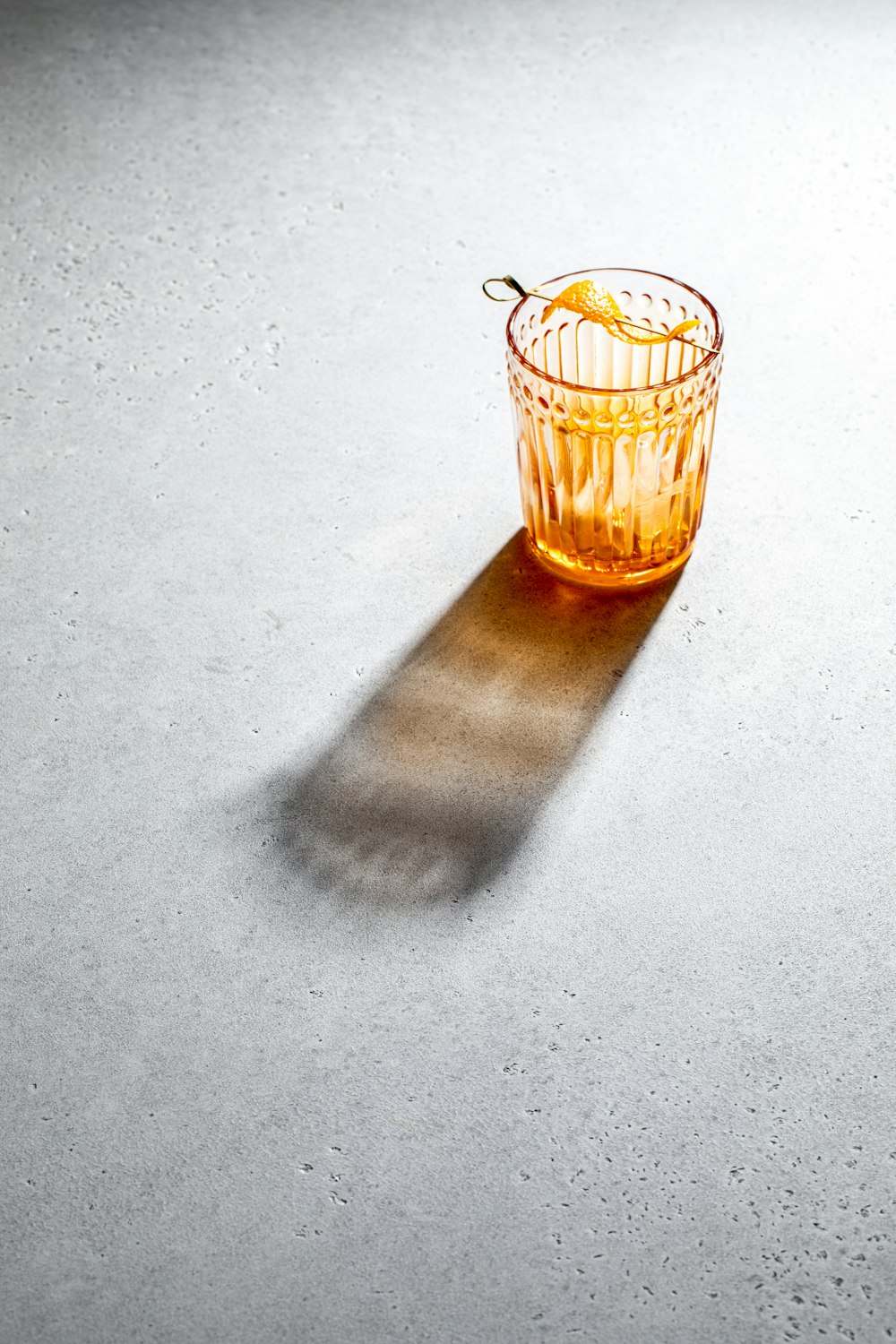 a glass of orange juice casting a shadow on the floor