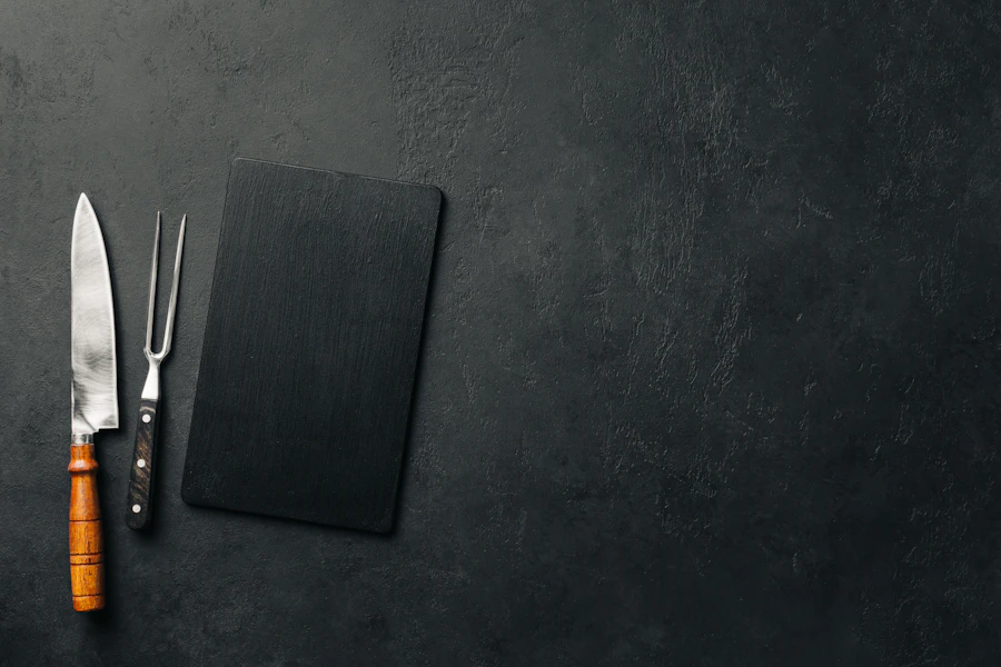 Top-down chef's knife, carving fork and black slate board on dark stone