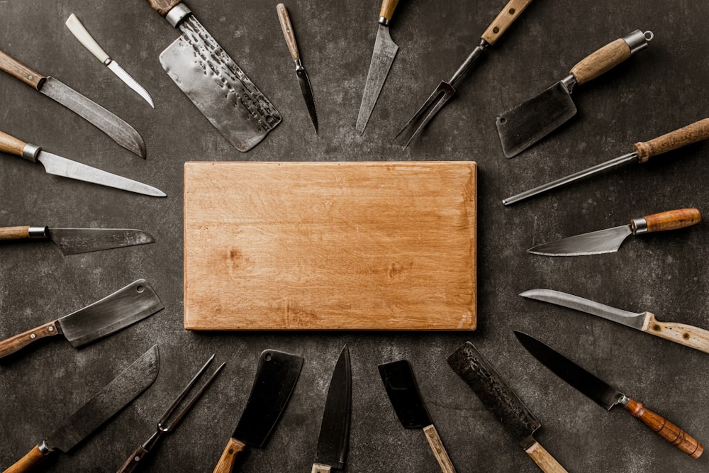 a wooden board surrounded by knives on a table