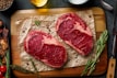 two steaks on a cutting board with herbs and spices