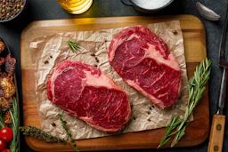 two steaks on a cutting board with herbs and spices