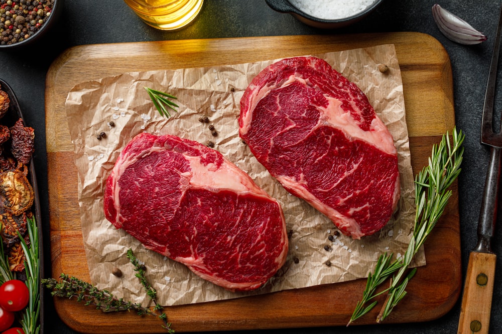 two steaks on a cutting board with herbs and spices