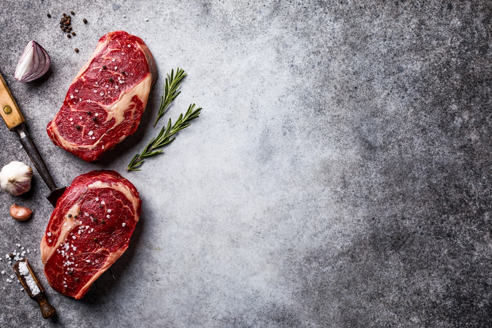 two raw steaks on a table with garlic and pepper