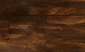 Dark wooden planks arranged horizontally with a textured surface, displaying a rich brown tone with subtle variations and natural grain patterns.