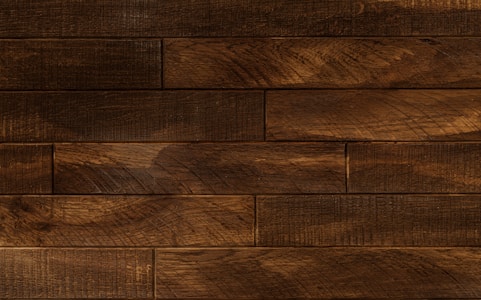 Dark wooden planks arranged horizontally with a textured surface, displaying a rich brown tone with subtle variations and natural grain patterns.