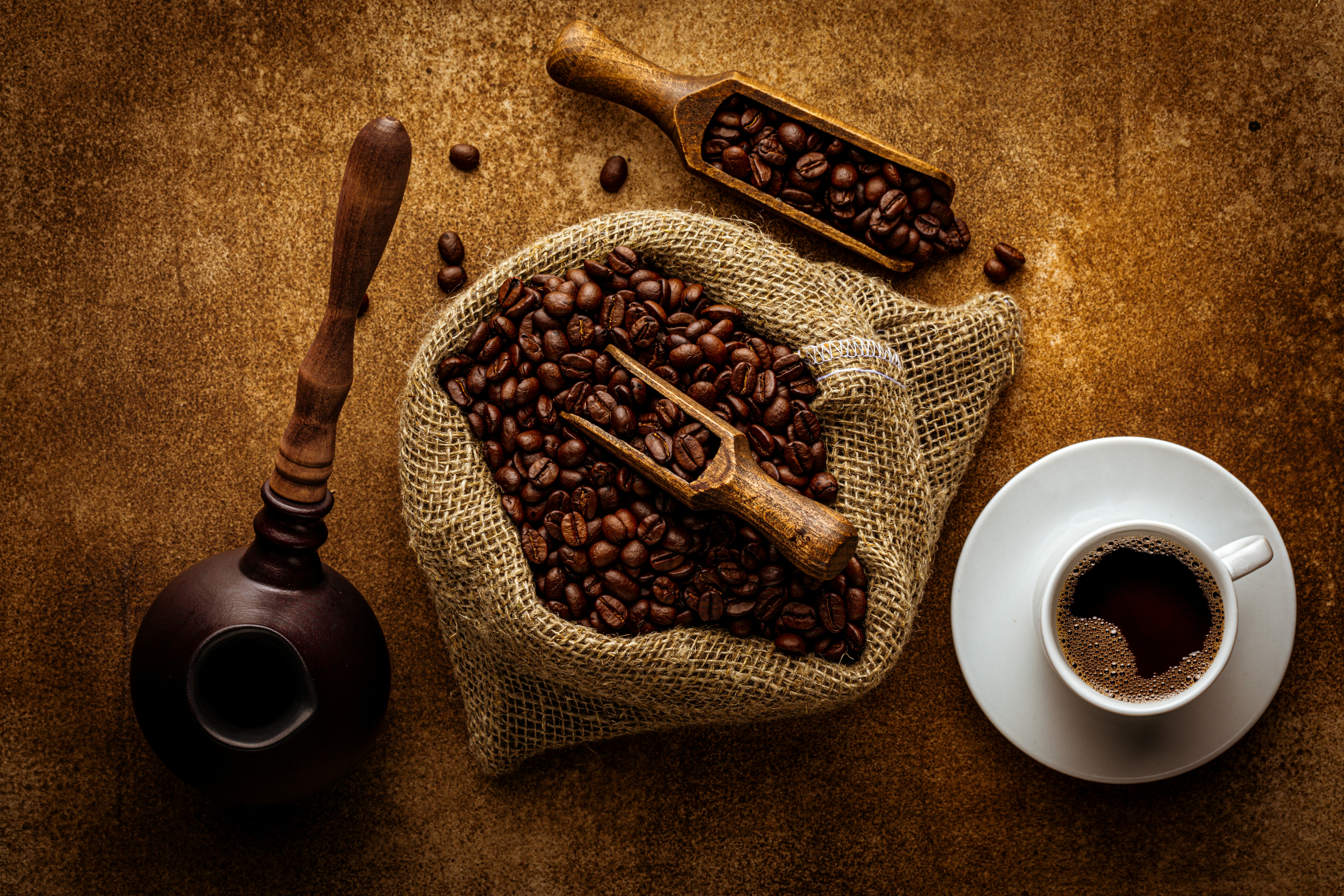 Coffee composition flat lay. Burlap sack with roasted organic coffee grains, freshly brewed americano drink in cup, cezve pot, wooden spoon over grunge background