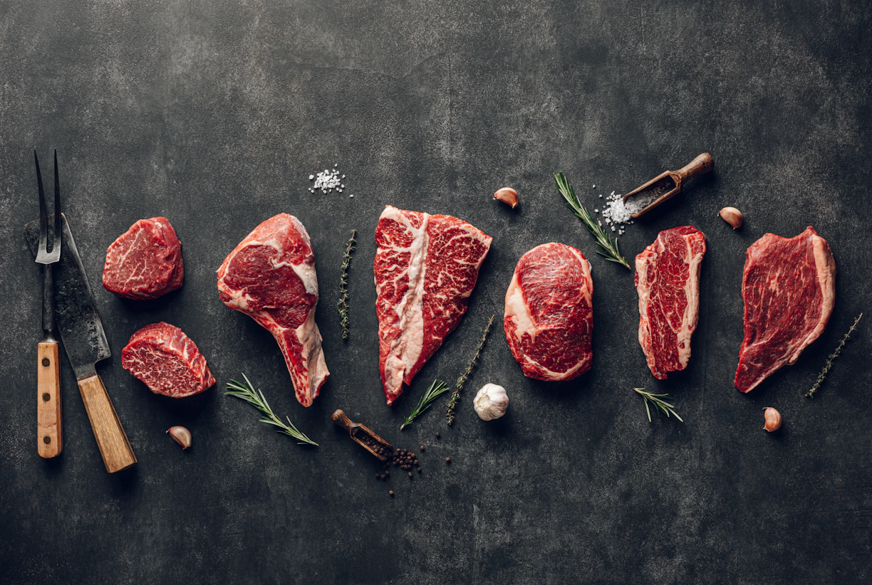 Cortes de carne de res cruda sobre mesa oscura coraw meat on a table with a knife, garlic and pepper
