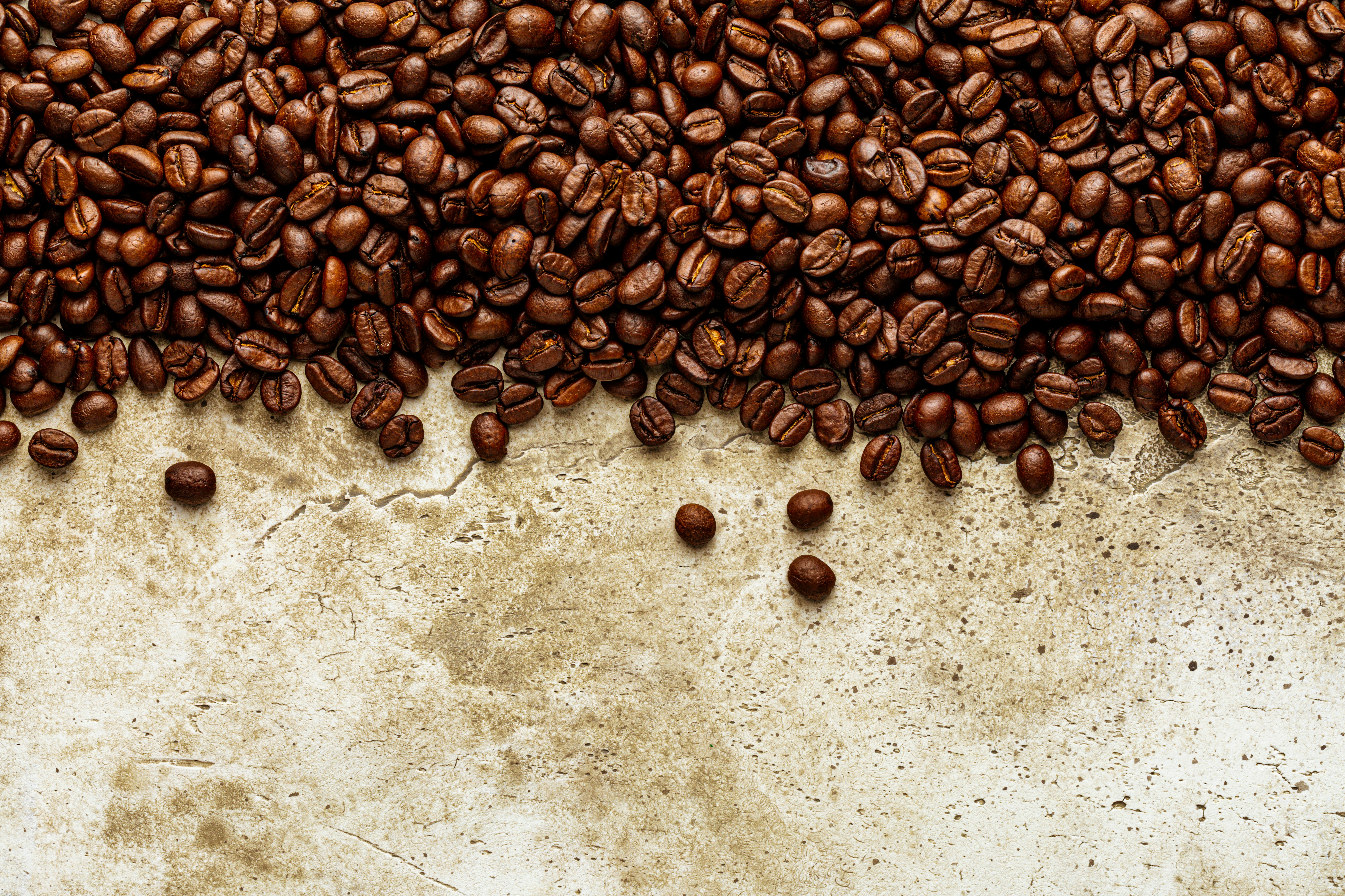 a pile of coffee beans sitting on top of a table, Roasted coffee beans over scratched stone wall texture. Top view on background copy space