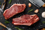 two steaks on a cutting board next to garlic, garlic, and a knife