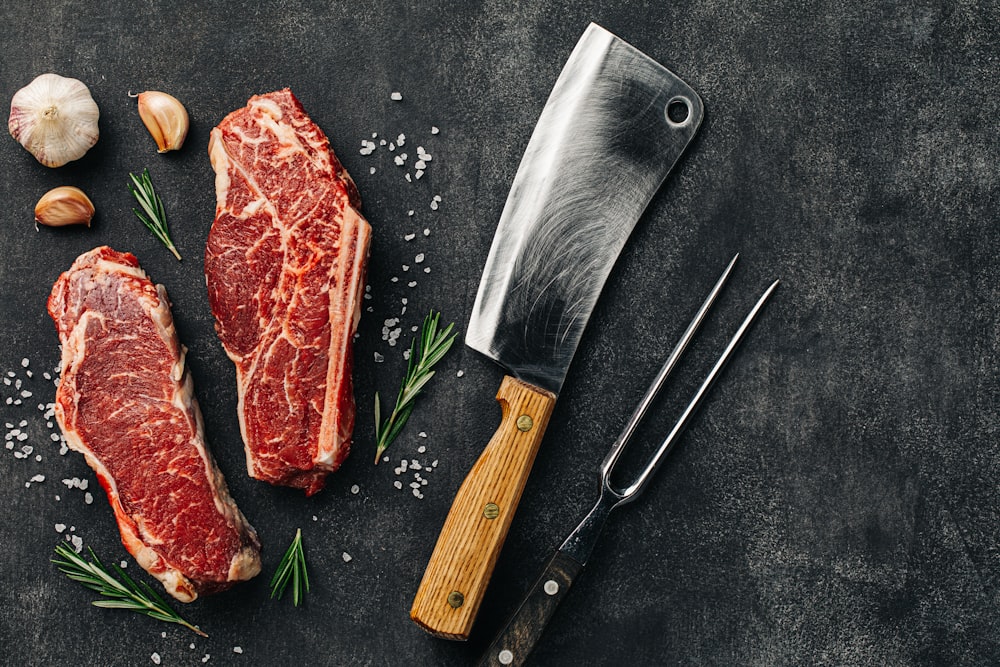 two pieces of raw meat next to a knife and garlic