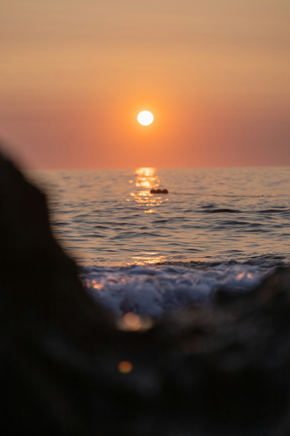 the sun is setting over the ocean with a boat in the distance