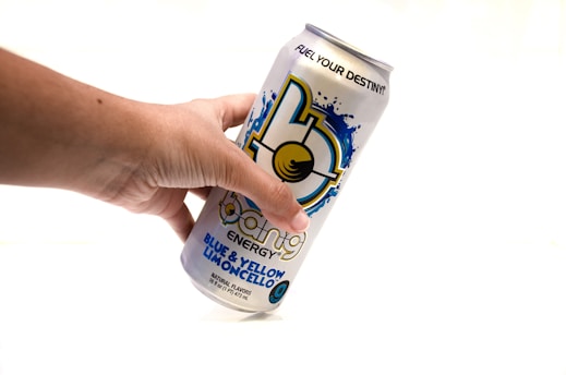 A hand is holding a can of Bang Energy drink, specifically the Blue & Yellow Limoncello flavor. The can features a bold, colorful design with a splash graphic and prominent branding.