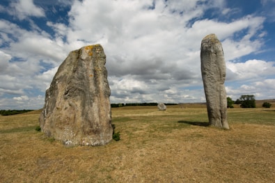 two large rocks in a grassy field under a cloudy sky