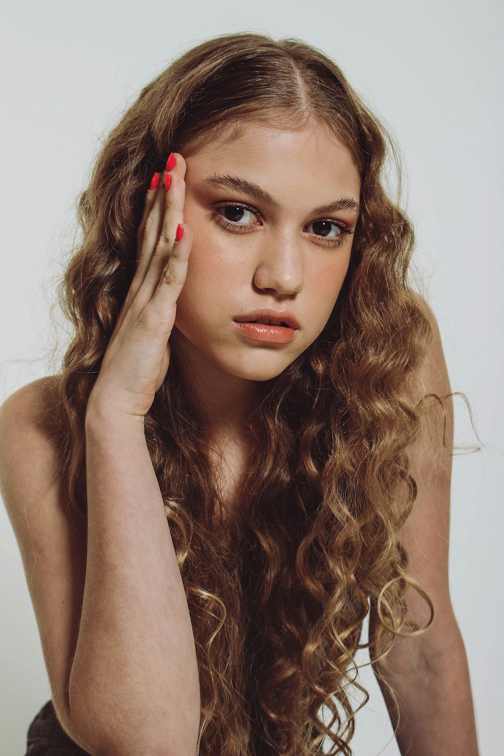 a woman with long curly hair holding her hand up to her face