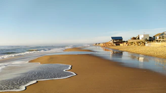 A cozy coastal beach house under a bright blue sky with gentle waves in the background.