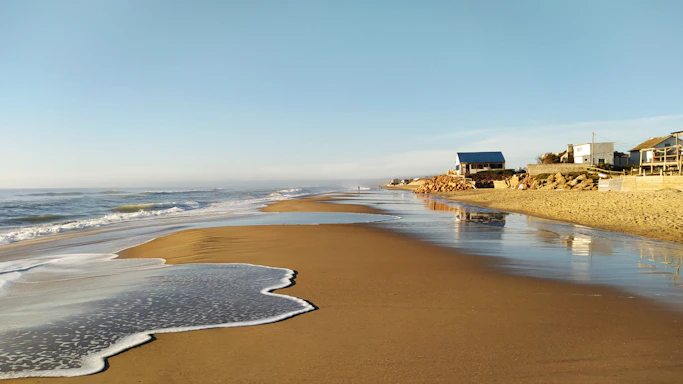 A cozy coastal beach house under a bright blue sky with gentle waves in the background.