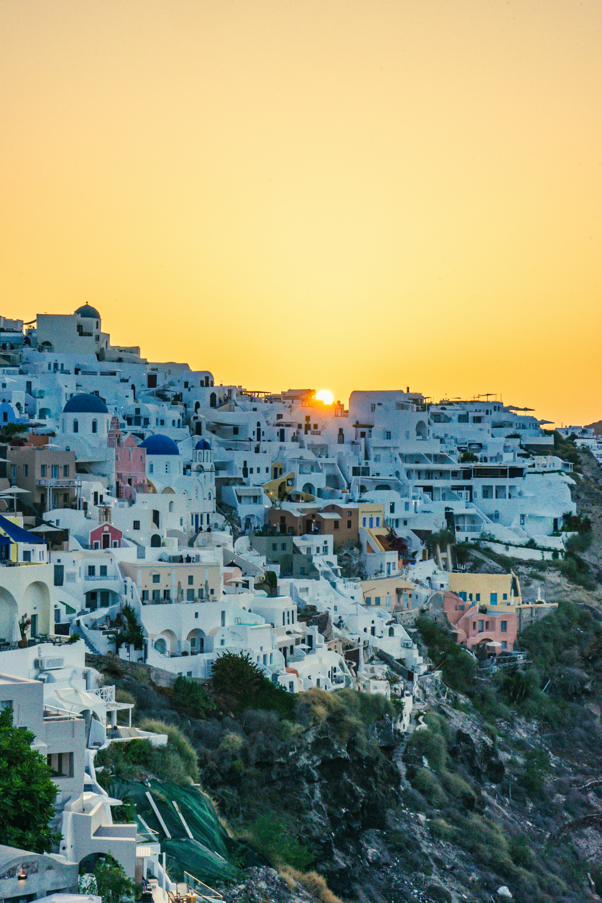 The iconic white-washed buildings and deep blue sea of a Greek island at sunset, casting warm golden hues.
