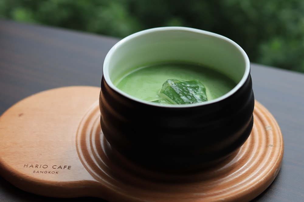 a cup of green soup on a wooden plate